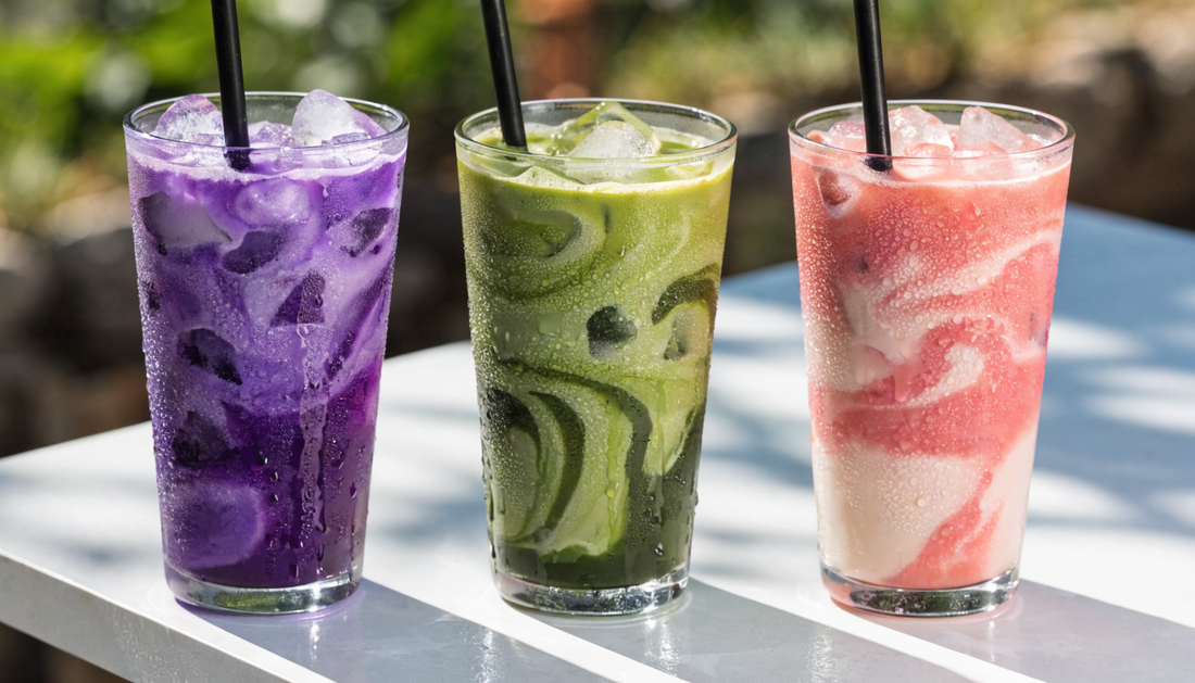 Trois lattes glacés colorés (ube violet, matcha vert, fraise rose) sur une table ensoleillée – Pure Tea
